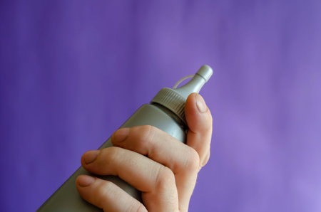 Male hand and gray plastic bottle of syrup. The man is holding a new bottle of sweet syrup for ice...