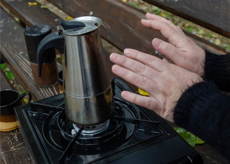 Tourism, travel concept. Women's hands warm themselves on the coffee machine on a portable outdoor...