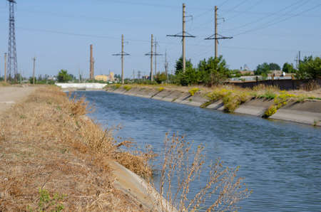 Irrigation agricultural channel with water. Power line along the canal for irrigation. Summer sunny day. Agribusiness.の写真素材