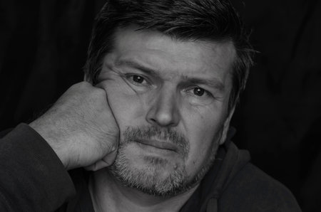 Body language concept. Black and white portrait of an adult man supporting his head with fist....
