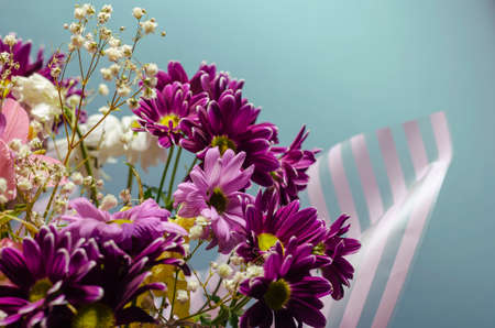 Bouquet of random flowers in striped wrapping on a light blue background. Purple and pink chrysanthemums close-up. Floristics, wedding bouquetの写真素材