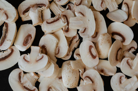 Group of raw champignons cut into pieces on black background. Food, ingredients.