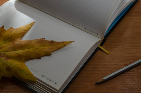 Creative background in the autumn theme. An open notebook, pencil, and fallen leaf on writing table....