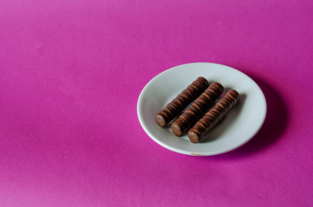 Three chocolates in white saucer on pink background. Sweet treats and candy wrapper on colored surface. Confectioneryの写真素材