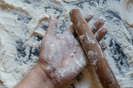 Wooden dough rolling pin in a man's hand on the kitchen table with white flour. Cooking home food concept. View from above at an angle.の写真素材