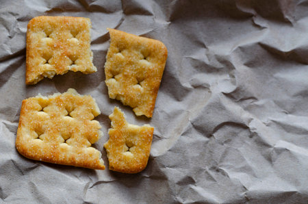 Square saltine cracker is broken into four random pieces. Pieces of snack crumpled-up wrapping...
