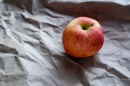 Red apple lies on crumpled wrapping paper. Side view from an angle. Selective focus.
