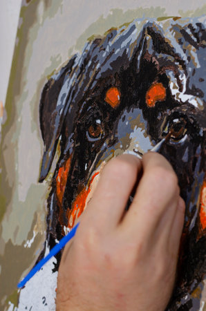 Concept of art, creativity and inspiration - man's hand with brush paints picture. Man paints portrait of Rottweiler on canvas. Close-up, selective focus.の写真素材