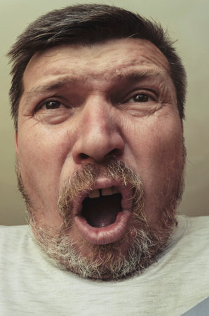 Unusual portrait of a bearded man with short brown hair. A grown man with gray stubble makes faces....