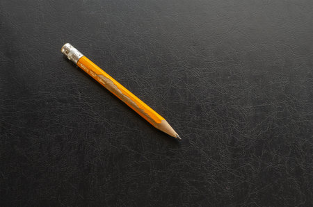 Close-up of an old yellow wooden pencil on black table. Engineering, accounting, business concept. Side view at an angle. Selective focus.の写真素材