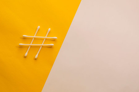 Cotton swabs in the shape of hashtag sign on white and yellow background. Minimalist conceptual...
