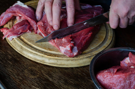 Cooking, meat recipes concept. Male hands chop with a knife Large pieces of fresh raw beef on a cutting board. Selective focus.の写真素材