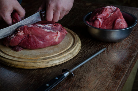 Cooking, meat recipes concept. Male hands chop with a knife Large pieces of fresh raw beef on a cutting board. Selective focus.の写真素材