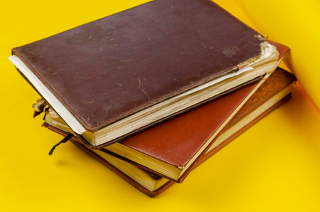 Stack of old diaries lying on yellow background. Diaries have worn pages. View from above at an angleの写真素材