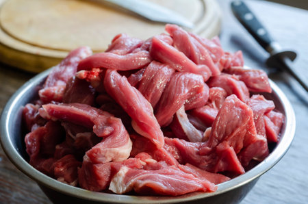 Cooking beef meat dishes. A portion of raw meat for beef stroganoff in a metal bowl. Cutting board, knife, mussat.の写真素材