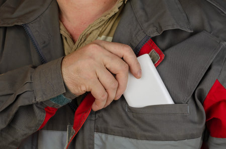 Close-up of a man's hand putting a white smartphone in his pocket. Man wearing special clothes for...