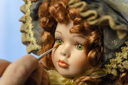 Hand carefully paints the doll's eye with a thin brush. Doll in a vintage style. Concept of combining work and hobbieの写真素材