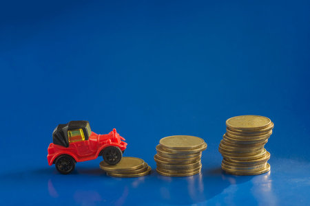 Auto insurance, transport and finance concept. Model of a toy retro car and a stack of coins on a blue background. Selective Focus.の写真素材