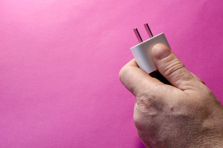 Man's hand holds white DC wall adapter against pink background. Replacement electrical plug for the...