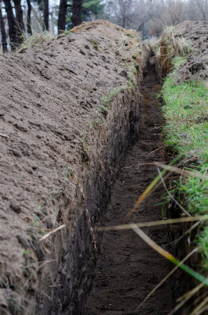 An empty long trench for a power cable is dug in the woods. Earthworks, underground utilities, industry. No people. Selective focus.の写真素材