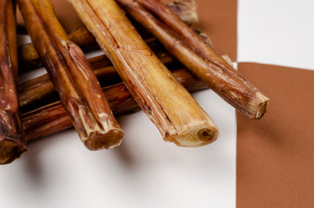 Useful dried chewy treats for pets in close-up. Dried bovine penis, bully sticks, beef pizzle for dogs on brown and white background. Focus on the foreground.の写真素材