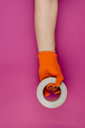 Handholds the roll of aluminum duct tape for padding. Man's hand with an orange glove on a pink background.の写真素材