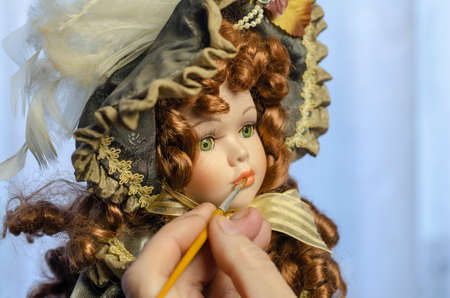Hand carefully paints the doll's lips with a thin brush. Doll in a vintage style. Concept of combining work and hobbyの写真素材
