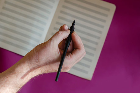A man's hand with a black fountain pen and opening music notebook on a purple background. Musical...