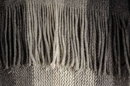 Close-up of fine-checked woolen texture in gray. Winter texture concept, fringe scarf, knitted clothing. Machine knitted woolen goods. Selective focus, noisy texture.の写真素材