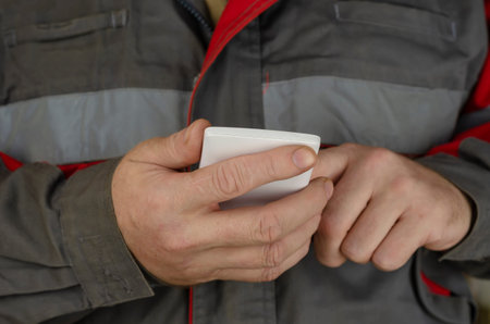 A man in special work clothes dials a phone number on a white smartphone. Special gray uniform with...