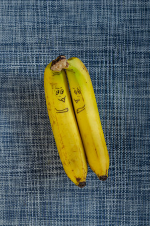 Lovers bananas on white and blue background. Two ripe bananas with drawn faces. Love, relationships. Selective focus.の写真素材