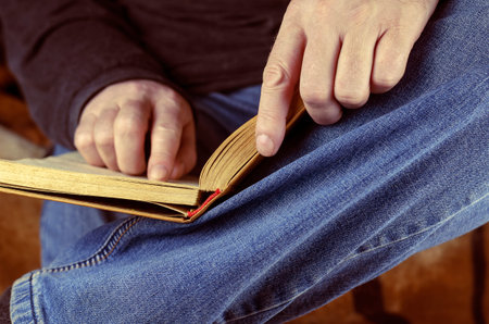 An old open book at his feet. A man is reading a book lying on his feet. Close-up, selective focus.の写真素材