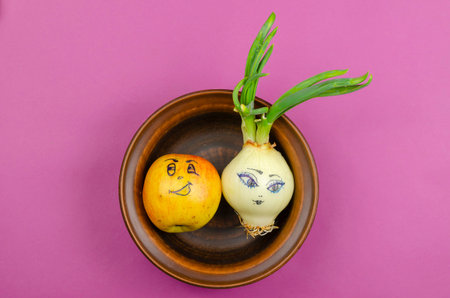 A funny white bulb with a woman's face and a Jolly Apple. Onion with green leaves and a red apple....