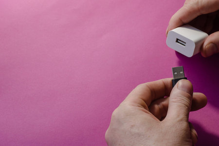 DC adapter and USB data cable in male hands. The male connects the black wire and the white US wall...