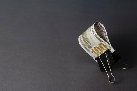 Creative abstract background with one hundred dollar bill clutched in a binder on a gray background....