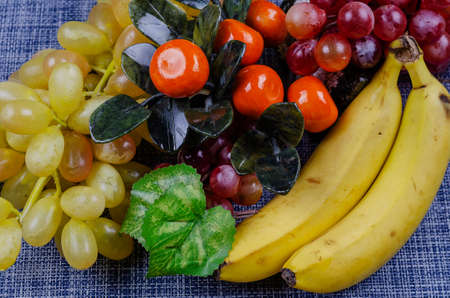 Still life with bananas, grapes and decorative tangerine tree. Berries and fruit close-up on white and blue background. Food, ingredients. Side view from an angle. Selective focusの写真素材