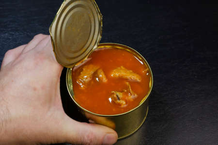 Canned food, shelf life food concept. Hand holds an open tin can with food in a tomato close-up. Selective focus.の写真素材