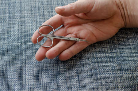 Manicure scissors lie in the open palm of an adult male. The hand rests on a blue surface. Close-up. Selective focus.の写真素材