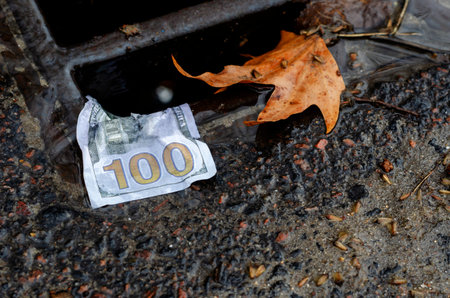 Money. American one hundred dollar bill on the edge of a storm drains grate after rain. Wet banknote...