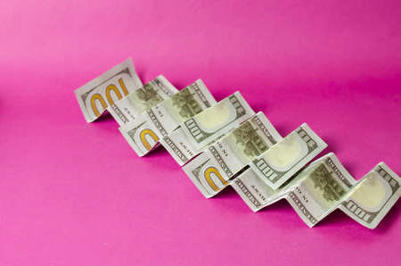 Accordion folded hundred dollar bills on a pink background. Abstract background with three banknotes.の写真素材