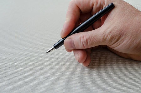 A man right-hand holds a fountain pen over a white table. Black fountain pen in adult man's hand....