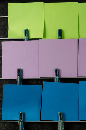 The paper sticky notes hanging from clothespins. Set of multicolored blank square stickers on black...