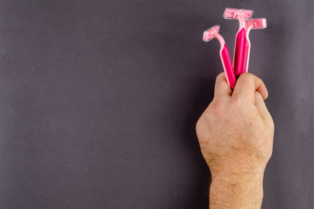 Handholds red plastic razors on a gray background. Three new women's razors in a man's hand. Top...