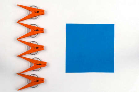 Brown plastic clothespins and blue paper square on a white background. A line of clothespins and a sticky note. Top view, flat layの写真素材