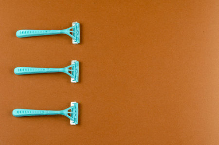 Blue plastic razors on a brown background. Three new razor. Top view, flat lay. Copy space