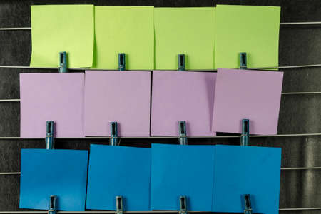 The paper sticky notes hanging from clothespins. Set of multicolored blank square stickers on black background. No people.の写真素材