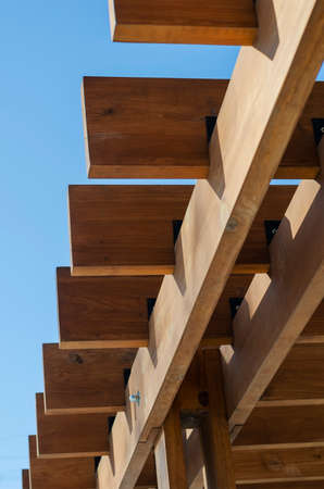 An abstract geometric composition of brown wooden planks against a blue sky. Fragment of an outdoor gazebo. Selective focus.の写真素材