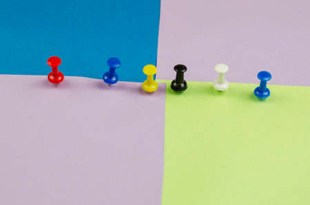 Push pins and lots of colorful sticky notes. Red, blue, yellow, black, white pushpins on a multicolored background. Side view at an angle. Selective focus.の写真素材