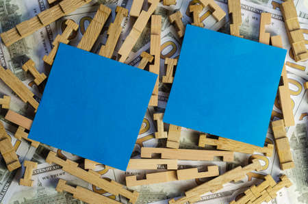 Two blue squares on top of a wooden puzzle and money. Blank paper stickers for notes and One hundred American dollar bills in the background. Finance, services, business, investments, rent, mortgage. Top view, Flat Lay,の写真素材