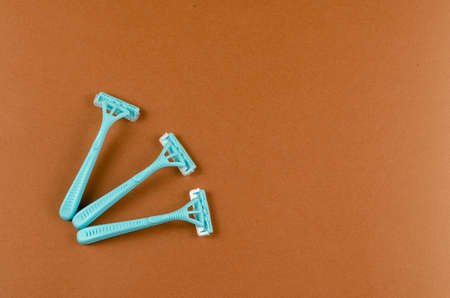 Blue plastic razors on a brown background. Three new razor. Top view, flat lay. Copy spaceの写真素材